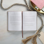 An open journal rests on a marble surface beside a beaded tassel, a gold tray holding a pink notebook, and a smartphone—setting the perfect scene for ten minutes of reflection with the Devotional 10 Minutes with God for Women Faux Leather by Christian Art Gifts during your daily quiet time.