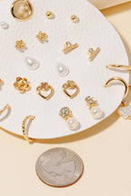 The Anarchy Street Mixed Styles Stud Earrings Set features assorted gold hoops and pearl studs on a white faux leather pad, displayed beside a quarter for size reference.