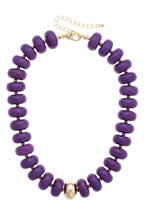 Canvas Style San Sebastián Beaded Resin Necklace: This statement piece showcases bold purple resin beads in large round shapes, accented with gold spacers, a single central gold bead, and an adjustable gold clasp chain.