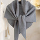 The JC Sunny Fashion Cashmere-Blend Knit Triangle Shawl with Cross-Front Design in gray is styled on a white hanger beside a cream sweater and large white faux flower, delivering chic elegance to any outfit.