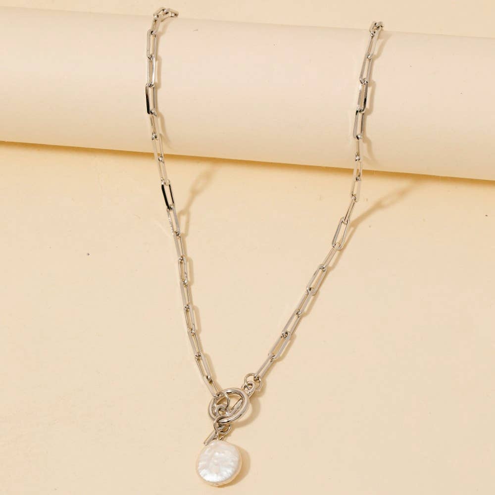 The Anarchy Street Toggle Chain Link Disc Pearl Charm Necklace, featuring elongated silver links and a round white pearl pendant, is displayed on a beige background.