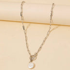 The Anarchy Street Toggle Chain Link Disc Pearl Charm Necklace, featuring elongated silver links and a round white pearl pendant, is displayed on a beige background.