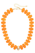 Introducing the San Sebastián Beaded Resin Necklace by Canvas Style: a statement piece adorned with large, round orange resin beads and highlighted by a single gold bead at the center, finished with a gold chain clasp.