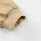 Close-up of a beige long-sleeve cuff from the Khaki Color Block Exposed Seam Long Sleeve Top by Shewin, displayed against a white background. The fabric appears soft and lightly textured, featuring elastic gathering that fits seamlessly into a khaki color palette. This item is an online exclusive.