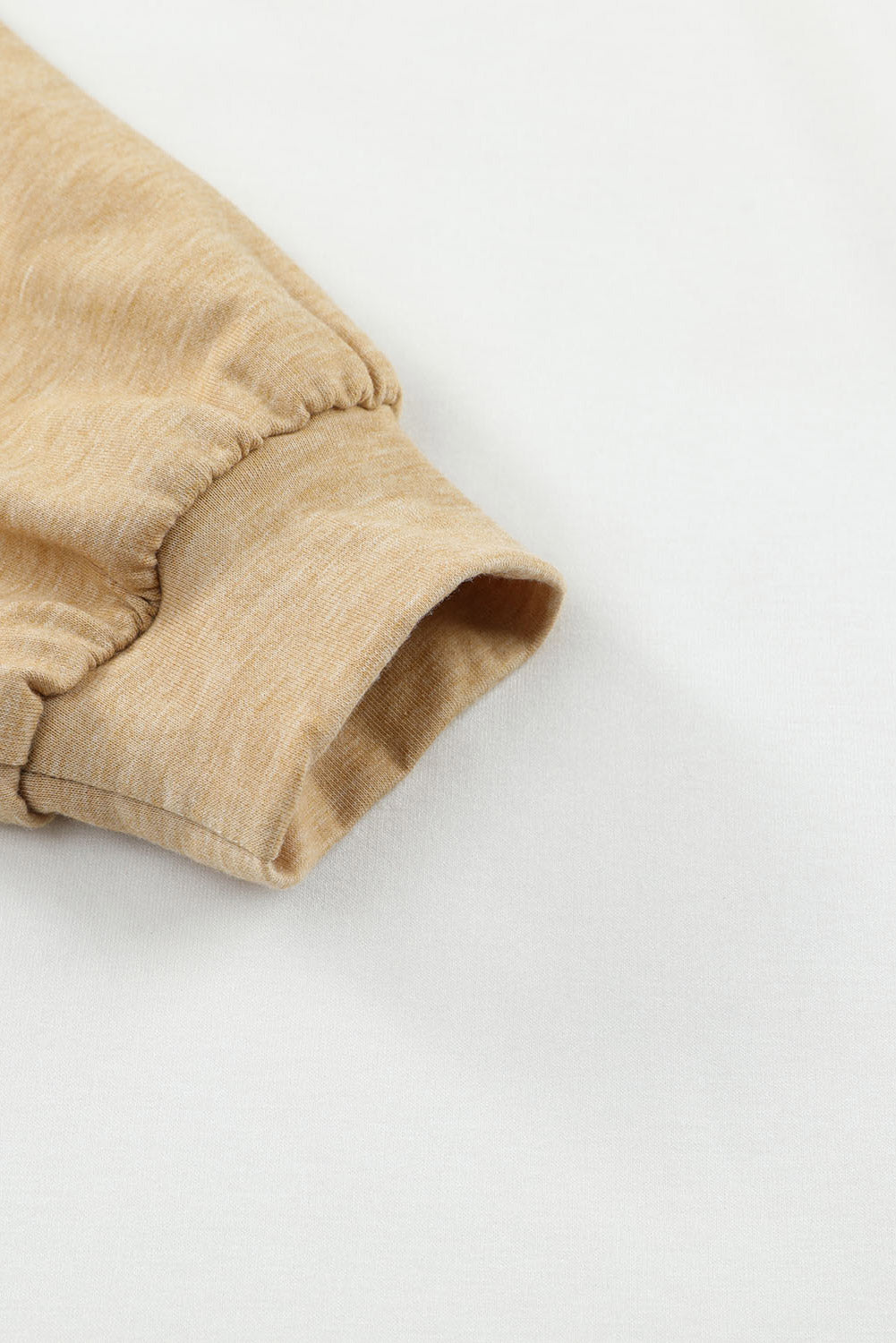 Close-up of a beige long-sleeve cuff from the Khaki Color Block Exposed Seam Long Sleeve Top by Shewin, displayed against a white background. The fabric appears soft and lightly textured, featuring elastic gathering that fits seamlessly into a khaki color palette. This item is an online exclusive.