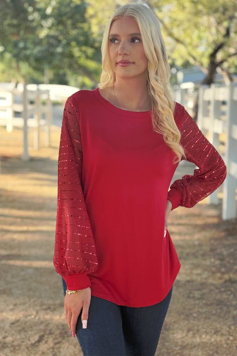 A woman stands outdoors in a 24-Hrs Fashion Sequin Sleeve Blouse and dark jeans, with a white fence and trees in the background.