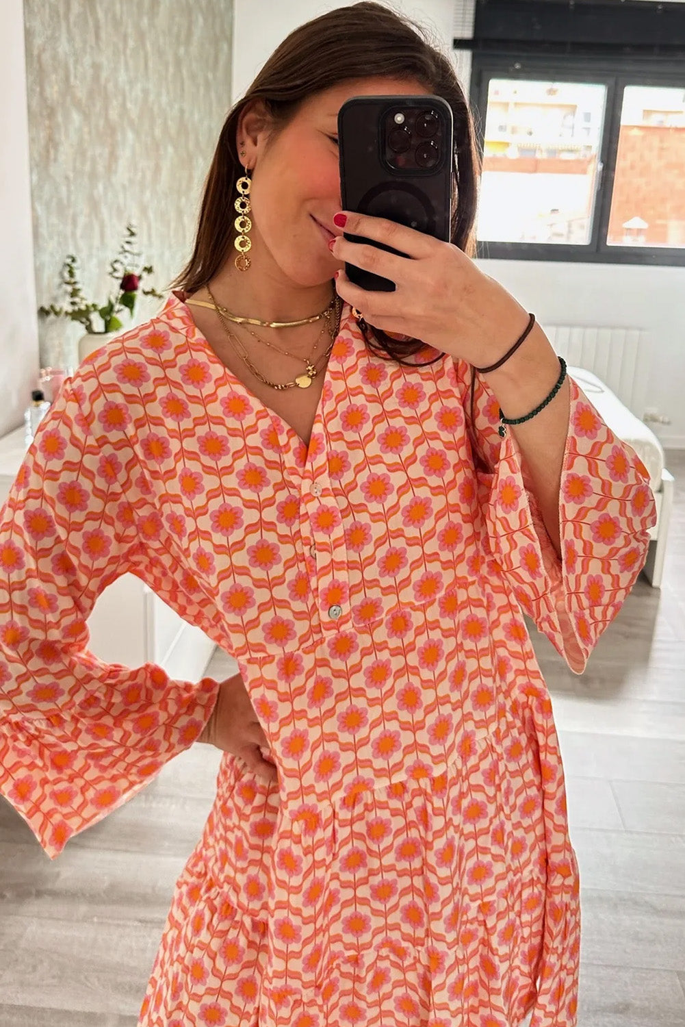 A person in a Shewin Orange Floral Button V Neck Bell Sleeve Mini Dress takes a mirror selfie in a room filled with flowers and sunlight streaming through the window.