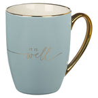 A light blue and cream ceramic coffee mug by Christian Art Gifts, this "It is Well with My Soul" mug features a gold handle and the phrase elegantly inscribed in gold script on the side.