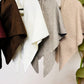 Four JC Sunny Fashion Cashmere-Blend Knit Triangle Shawls with Cross-Front Design in brown, white, gray, and beige hang on black hangers. Each stylish piece doubles as a cozy scarf. A plant is partially visible on the right side.