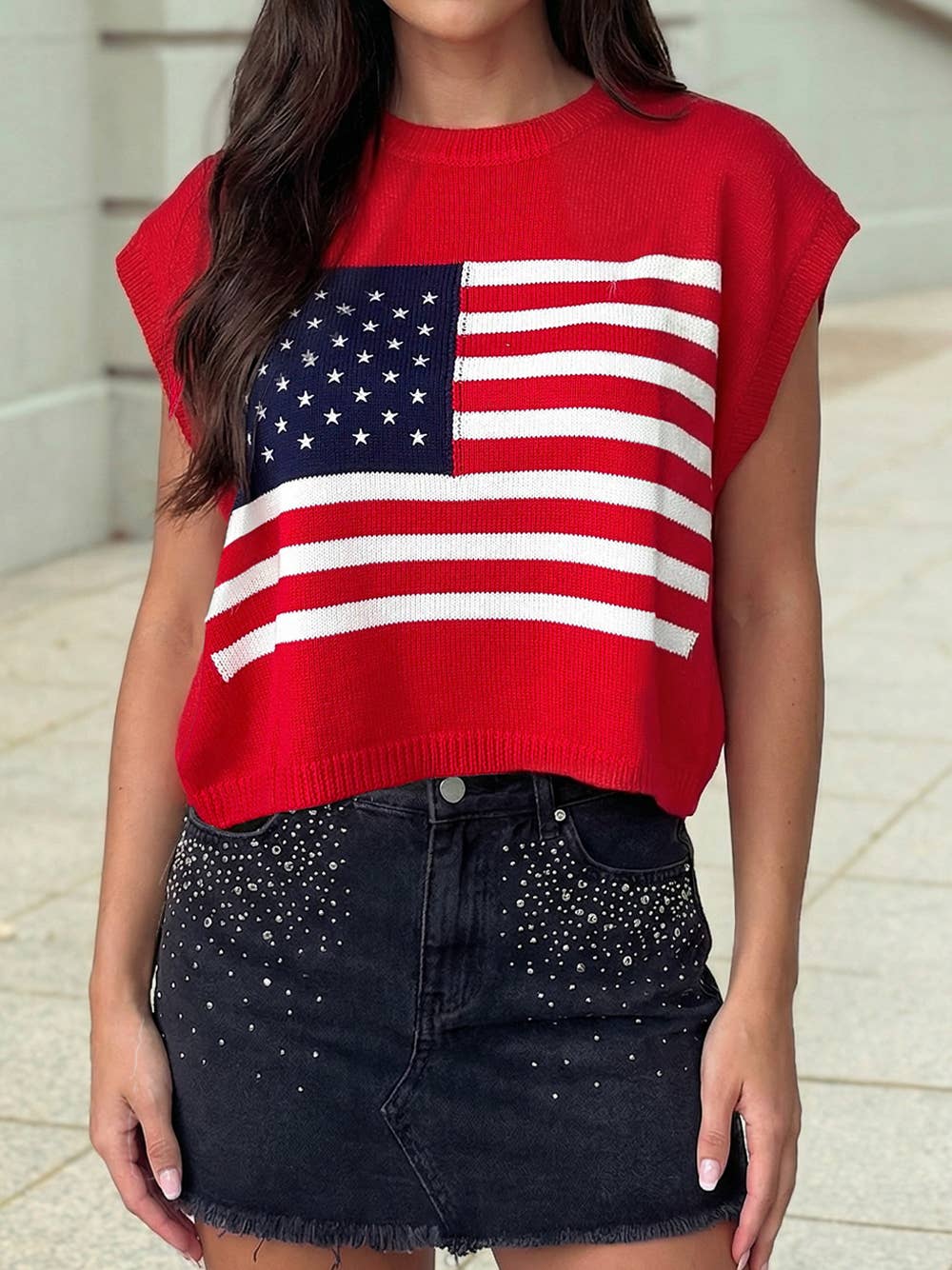 A person is wearing the 4th of July Stars and Stripes Dolman Short Sleeve Sweater by 1 the Woman with a black studded denim skirt, standing outdoors.