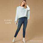 Woman in a light blue Lightweight Ponchos Wrap by COCO + CARMEN over a white top and jeans, standing against a beige background. Text: "FLOWY CAPE" and “Lightweight Poncho Shown in Powder Blue”—ideal for layering.