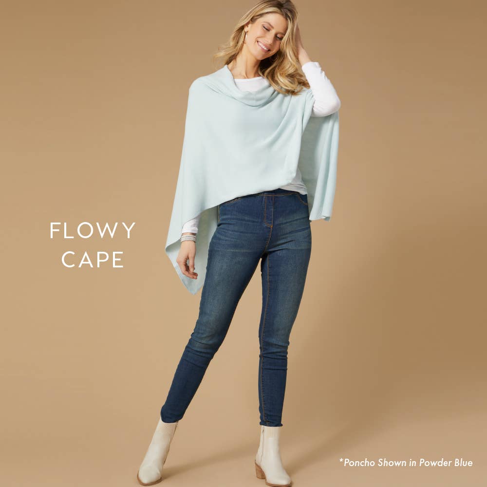 Woman in a light blue Lightweight Ponchos Wrap by COCO + CARMEN over a white top and jeans, standing against a beige background. Text: "FLOWY CAPE" and “Lightweight Poncho Shown in Powder Blue”—ideal for layering.