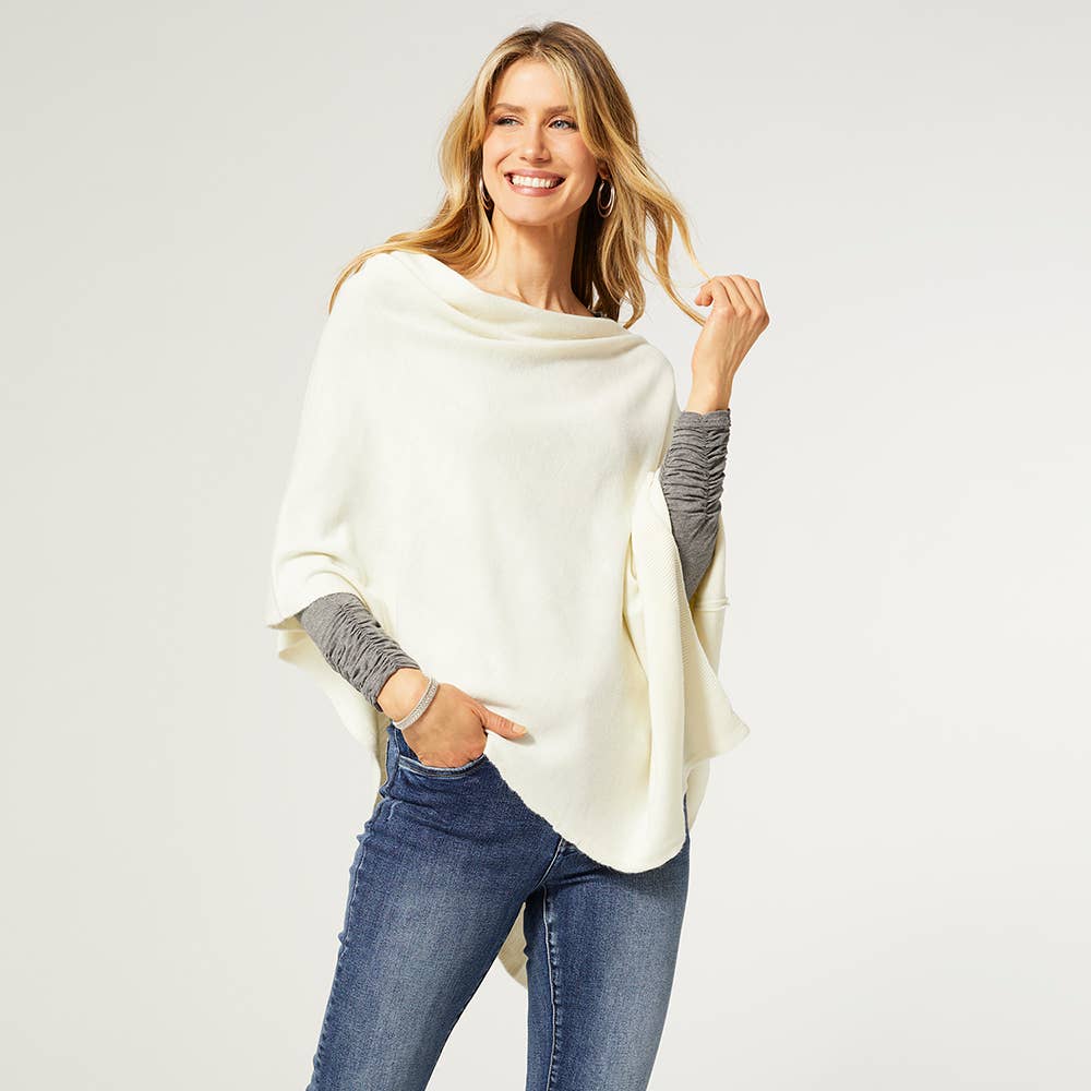 A woman models the COCO + CARMEN Lightweight Ponchos Wrap over a gray long-sleeve shirt and blue jeans, smiling against a plain light background—ideal for layering your wardrobe.