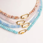 Four beaded necklaces from WJW, in pastel pink, beige, and blue tones, each featuring a gold-colored carabiner clasp closure, are arranged side by side on a white surface. Included in the collection is the Stainless Steel Turquoise Chunky Bead Carabiner Necklace, which introduces a subtle pop of color with its turquoise beads.