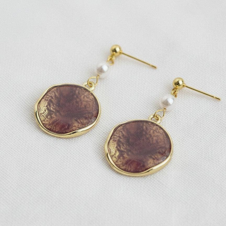 A pair of Ellemadera Purple Enamel Geometric Drop Earrings, featuring vintage-inspired gold-tone shapes with round, marbled brown pendants and delicate white pearl accents, elegantly finished with enamel and displayed on a white surface.