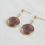 A pair of Ellemadera Purple Enamel Geometric Drop Earrings, featuring vintage-inspired gold-tone shapes with round, marbled brown pendants and delicate white pearl accents, elegantly finished with enamel and displayed on a white surface.
