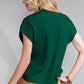 A blonde woman stands with her back turned, wearing Shewin's green Patch Pocket Ribbed Knit Short Sleeve Sweater and brown pants, ideal for transitional weather.