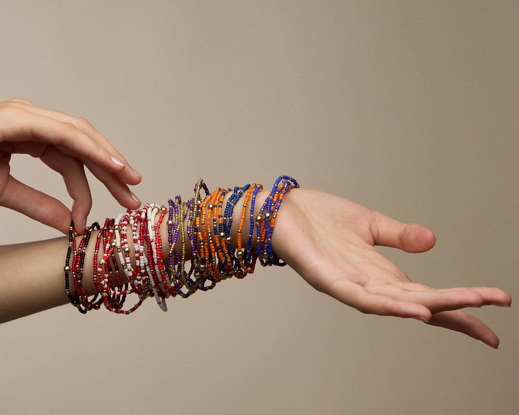 A person’s wrist and forearm wearing a Game Day Seed Beaded Bracelet Set in shades of black, white, red, purple, orange, and blue.