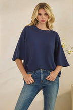 Woman wearing a navy blue CLOUDY KNIT 3/4 SLEEVE ROUND NECK TOP with three-quarter length wide sleeves and blue jeans.