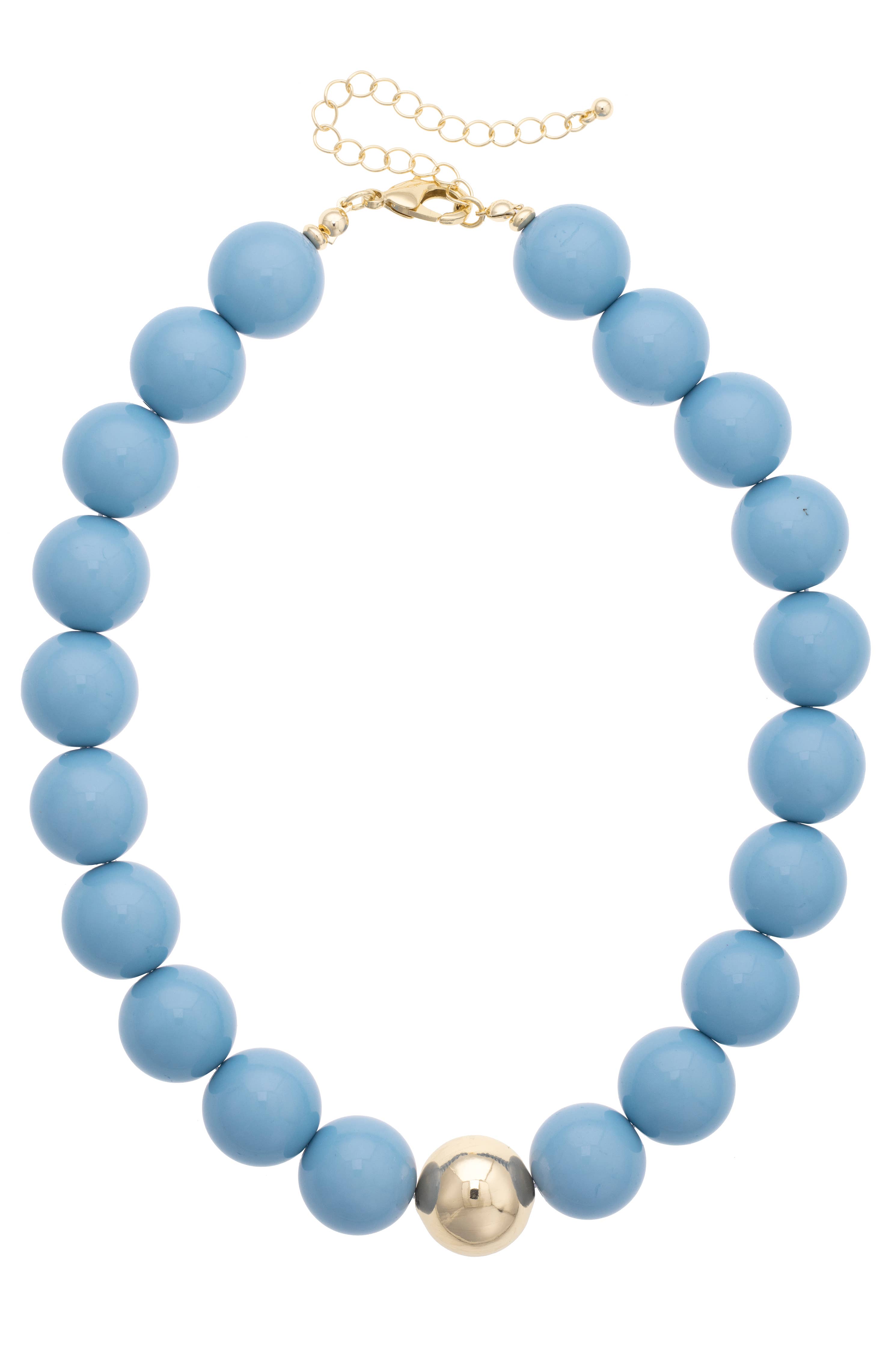 Introducing the Marjorie Game Day Beaded Necklace by Canvas Style—a bold statement piece featuring round blue beads and a single oversized gold bead at the center, finished with a gold clasp and an adjustable chain for versatile wear on any occasion.