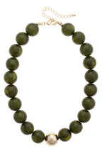 The Marjorie Fall Beaded Necklace by Canvas Style features oversized, round dark green resin beads accented with a single shiny gold bead at the center, finished with a gold clasp and adjustable chain.