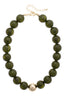The Marjorie Fall Beaded Necklace by Canvas Style features oversized, round dark green resin beads accented with a single shiny gold bead at the center, finished with a gold clasp and adjustable chain.