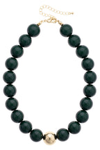 The Marjorie Game Day Beaded Necklace by Canvas Style features oversized, glossy black beads with a bold central gold bead, finished with a gold clasp and adjustable chain—making it the perfect statement necklace for any occasion.