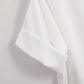 Close-up of the White Relaxed Short Sleeve Blouse by Rosa Clothing, showcasing folded cuff details and a chic, easygoing style against a light background.