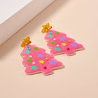 Add some specifics to highlight the product name and brand. Here’s a rewritten version: The Glittery Christmas Tree Drop Earrings by Lilla Haven are crafted from sparkling pink acrylic and adorned with colorful star and bead accents, making them the perfect holiday statement piece. Each earring is topped with a cheerful yellow star, beautifully displayed on a light beige surface.