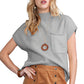 She opts for the Patch Pocket Ribbed Knit Short Sleeve Sweater by Shewin, pairing it stylishly with a brown buttoned skirt and a circular pendant necklace for an effortlessly chic look perfect for transitional weather.