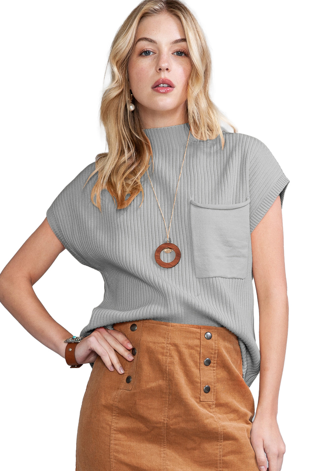 She opts for the Patch Pocket Ribbed Knit Short Sleeve Sweater by Shewin, pairing it stylishly with a brown buttoned skirt and a circular pendant necklace for an effortlessly chic look perfect for transitional weather.