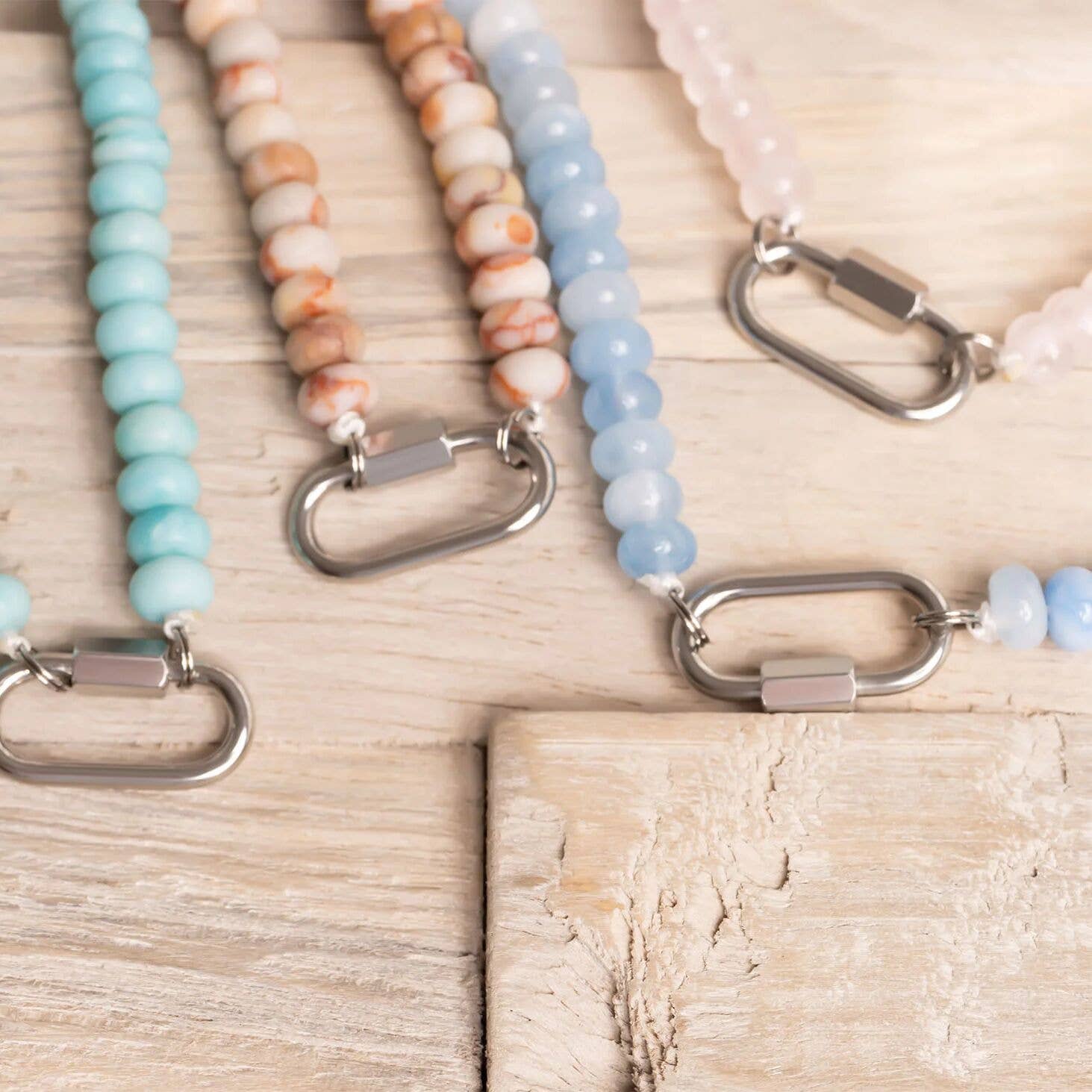 Four pastel-colored beaded keychains with silver clasps are displayed on a light wooden surface, beautifully complementing the soothing tones of the WJW Stainless Steel Turquoise Chunky Bead Carabiner Necklace.