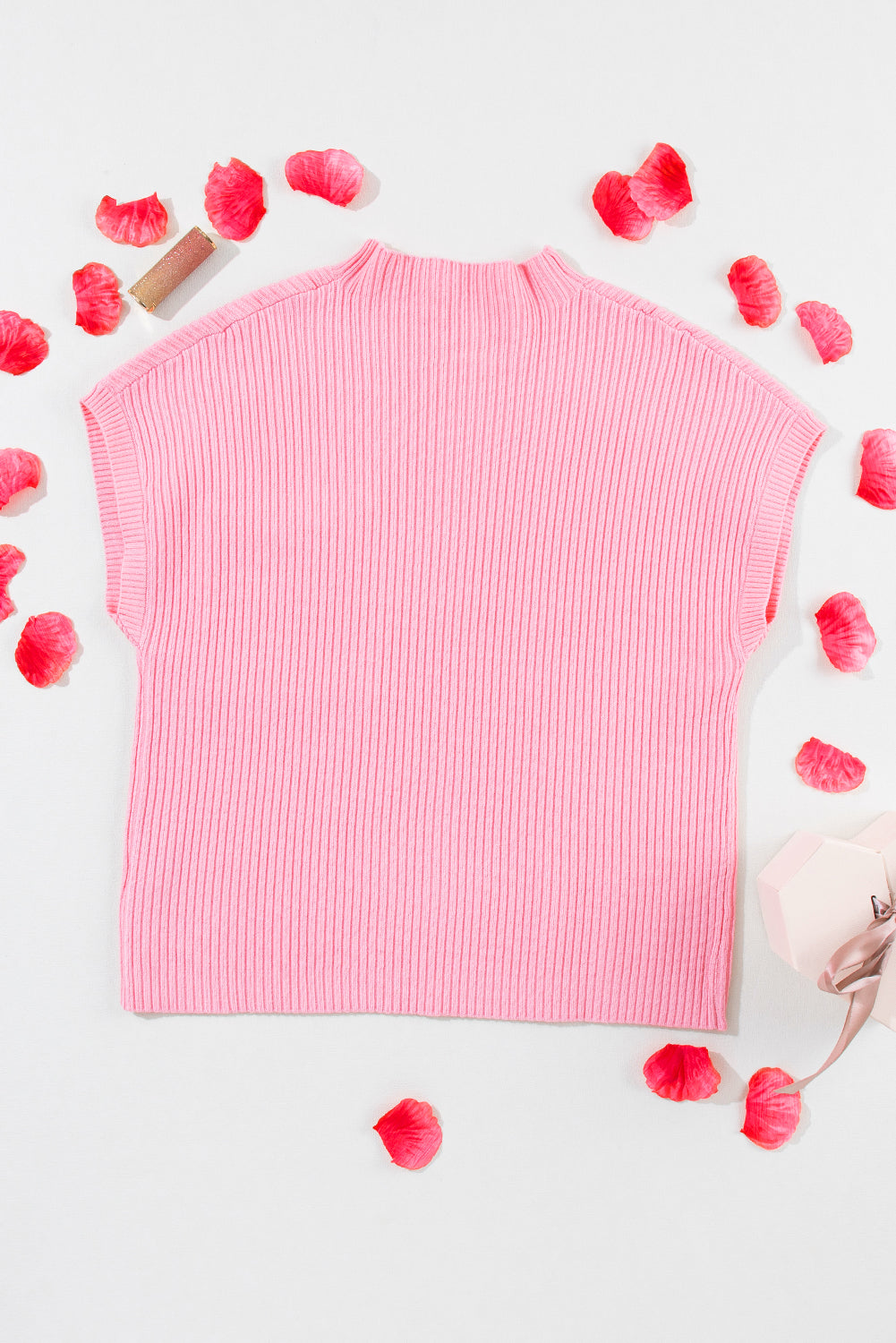 The Shewin Patch Pocket Ribbed Knit Short Sleeve Sweater in pink lies flat amidst scattered rose petals on a white background, offering charm and elegance for transitional weather with its soft knit fabric.