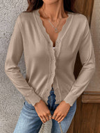 A person wearing the Suhkasana Women’s Solid Color V-Neck Lettuce Edge Knit Cardigan in light beige over a white top and blue jeans, standing against a textured wall.