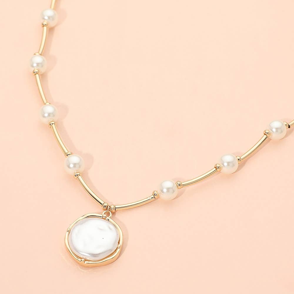 The Round Pearl Pendant Station Necklace by Sensibling Corp. features a delicate beaded chain adorned with small white pearls spaced along its length and a larger, round pearl pendant set in gold. The necklace includes an adjustable extender for the perfect fit and is shown against a light peach background. Main image