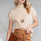 A person wearing sunglasses pairs the Shewin Patch Pocket Ribbed Knit Short Sleeve Sweater in beige with a brown knit skirt and a chic brown leather clutch, effortlessly embracing transitional weather.