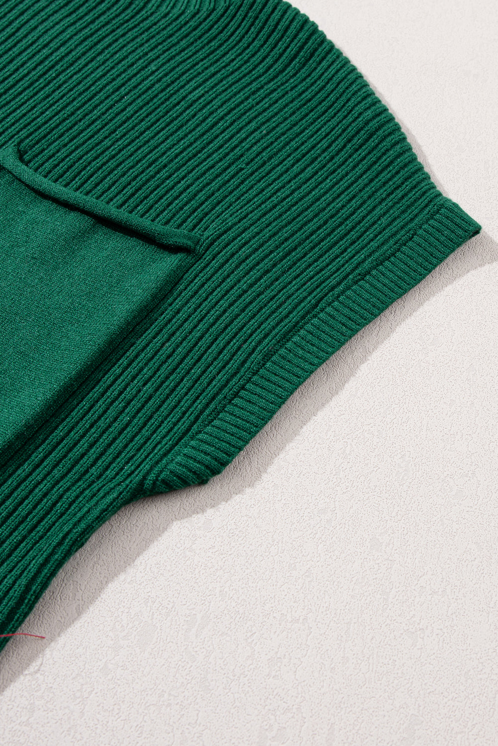 Close-up of a sleeve and pocket from the versatile Shewin Patch Pocket Ribbed Knit Short Sleeve Sweater in green, displayed on a light textured surface, ideal for transitional weather.