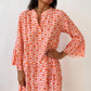 A person smiles while posing in a Shewin Orange Floral Button V Neck Bell Sleeve Mini Dress against a plain white background.