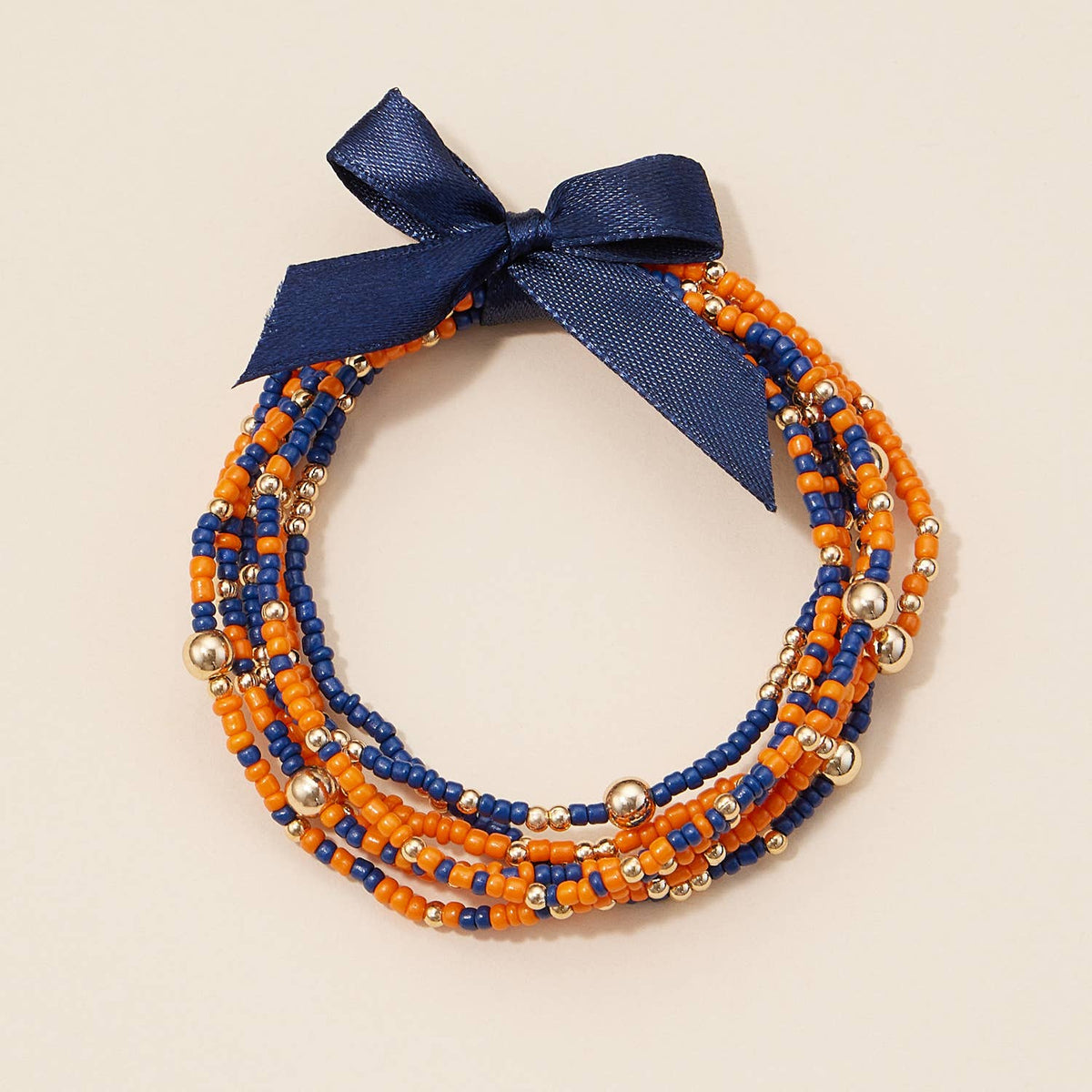 Game Day Seed Beaded Bracelet Set featuring a stack of orange and blue beaded bracelets with gold-toned metallic accents and a navy blue ribbon bow.
