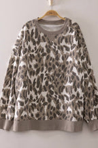 The Leopard Printed Crew Neck Sweatshirt by very J features a stylish gray and beige leopard print, long sleeves, and ribbed cuffs, hem, and neckline. Displayed on a wooden hanger against a light-colored wall, its relaxed fit offers effortless style.