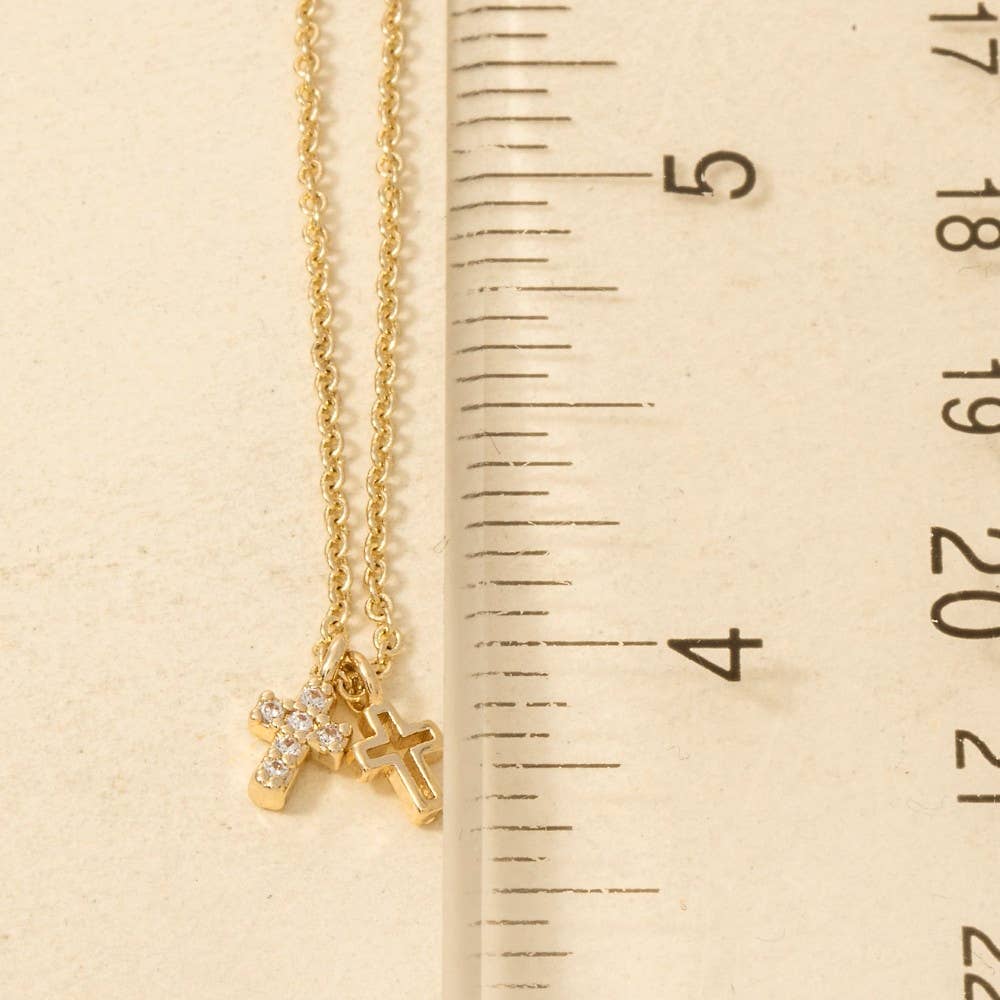 Two Secret Box Gold Dipped CZ Cross Pendant Necklaces by Anarchy Street sit beside a ruler for scale, featuring small gold cross pendants—one larger brass pendant adorned with sparkling stones.
