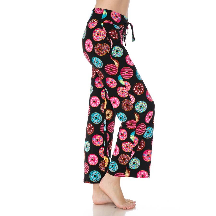 A person stands barefoot in Leggings Depot's Buttery Soft Print Pajama Pants, featuring a colorful donut pattern and comfy elastic waistband, shown from the side against a white background.