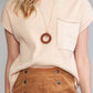 A person elegantly wears the Shewin Patch Pocket Ribbed Knit Short Sleeve Sweater in beige, accessorized with a circular pendant necklace, perfectly pairing it with a brown buttoned skirt for transitional weather.