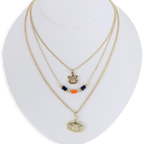 The Auburn Gold & Tube Bead Trio Necklace Set by Seasons Jewelry features three gold-tone layered necklaces displayed on a white bust, showcasing an AU logo, navy and orange tube bead accents, and an oval pendant with a raised design—an ideal War Eagle accessory for spirited Auburn University fans.