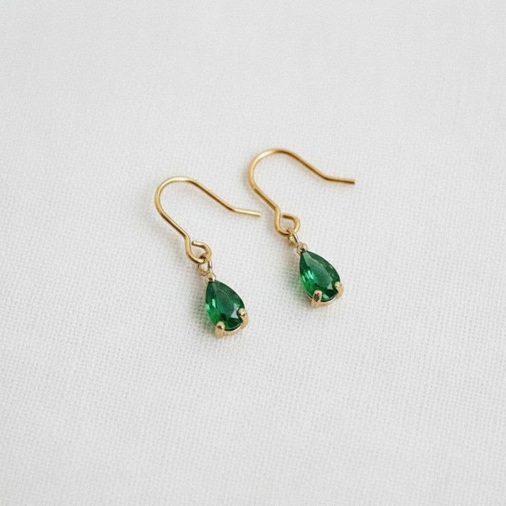 A pair of Ellemadera Chic Gemstone Dangle Earrings, featuring teardrop-shaped green gemstones and hypoallergenic gold settings, displayed on a white fabric background.