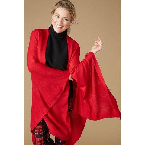 A woman smiles against a plain beige background, wearing a black turtleneck, red plaid pants, and the Kiara Lightweight Wrap by COCO + CARMEN layered on top.