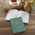 A teal Devotional Be Still and Know Faux Leather Teal resting on an open book next to a cup of coffee and flowers.