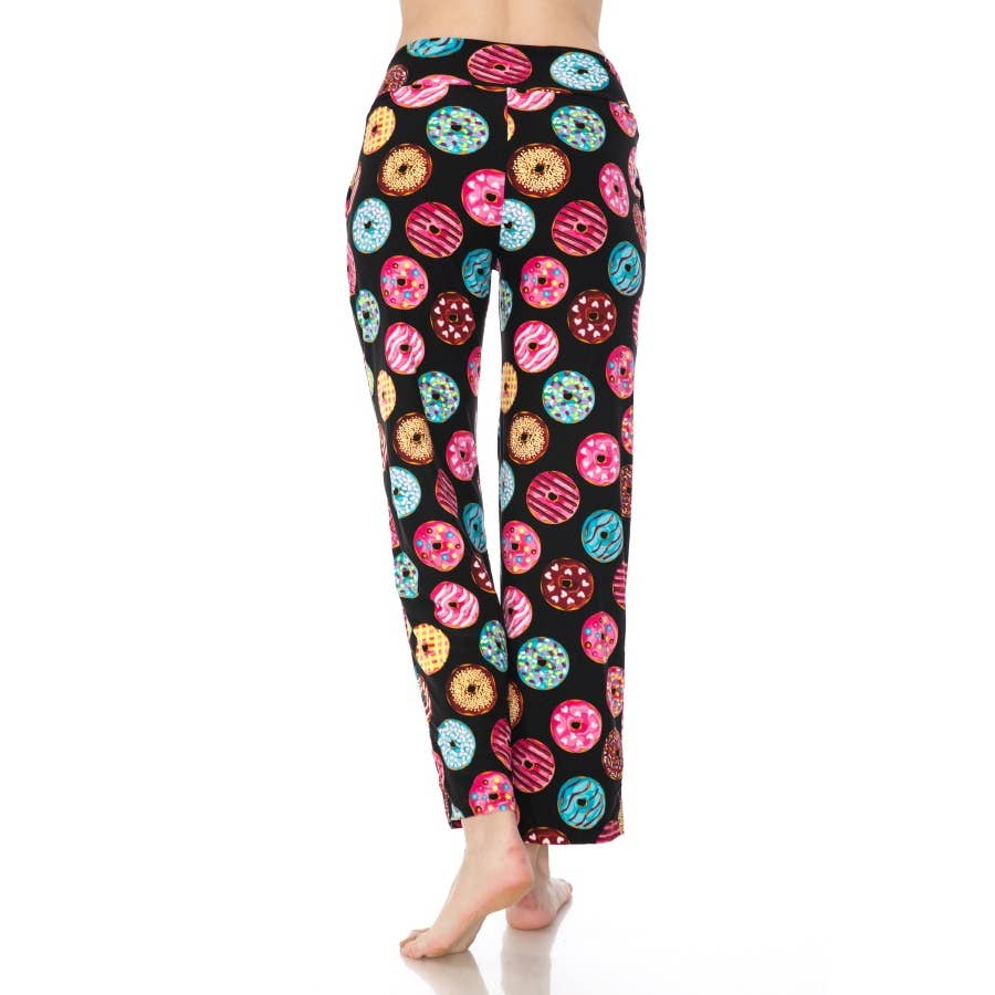 A person stands barefoot against a white background wearing Leggings Depot Buttery Soft Print Pajama Pants featuring a colorful donut pattern and an elastic waistband.