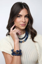 A woman wearing a Palermo Resin Beaded Necklace and matching blue layered resin beaded bracelet.