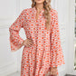 A woman in a Shewin Orange Floral Button V Neck Bell Sleeve Mini Dress smiles while standing indoors, holding a round woven bag.